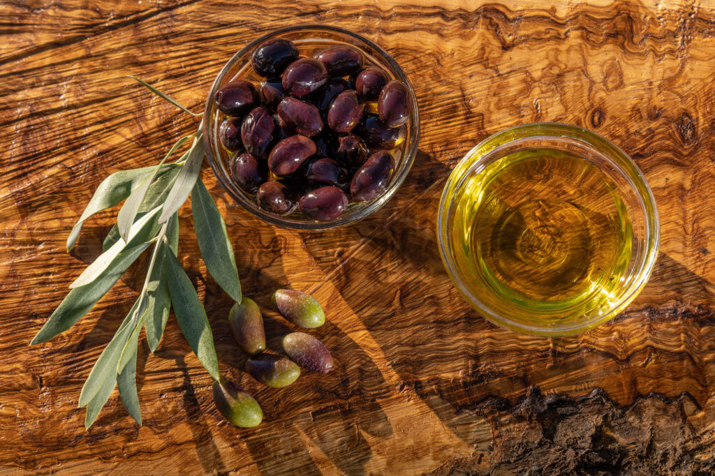 Productfoto van olijven en een bakje olijfolie op een plankje van olijfhout.