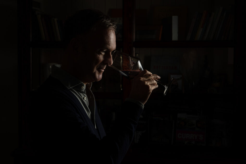 Close up portretfoto van wijnhandelaar, die ruikt aan een glas rode wijn. Rotterdam.